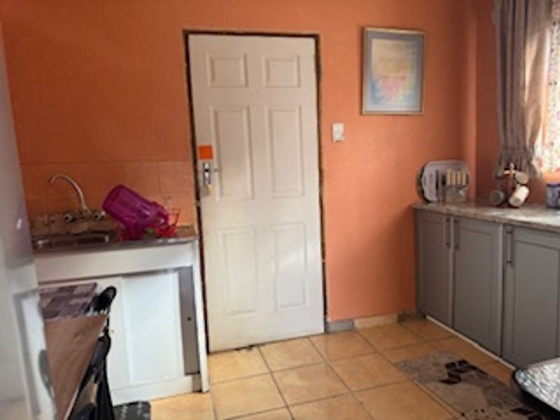 A compact kitchen featuring built-in cabinetry, laminate countertops, and tiled flooring, currently finished in a dated orange wall color.