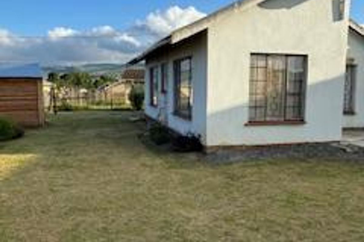 Rear view of the property showing the exterior wall, security-barred windows, and a surrounding lawn area.