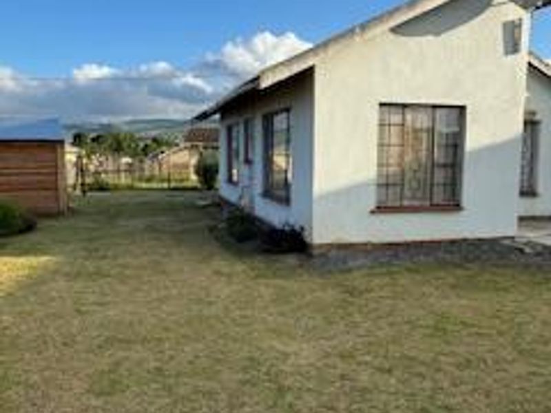 Rear view of the property showing the exterior wall, security-barred windows, and a surrounding lawn area.