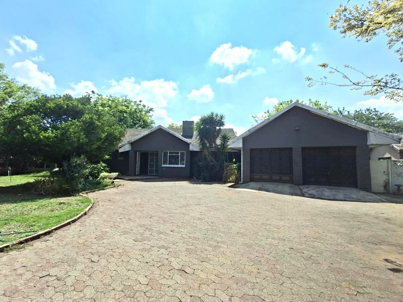 Front view of a residential property featuring a double garage, paved driveway, and established garden surroundings.