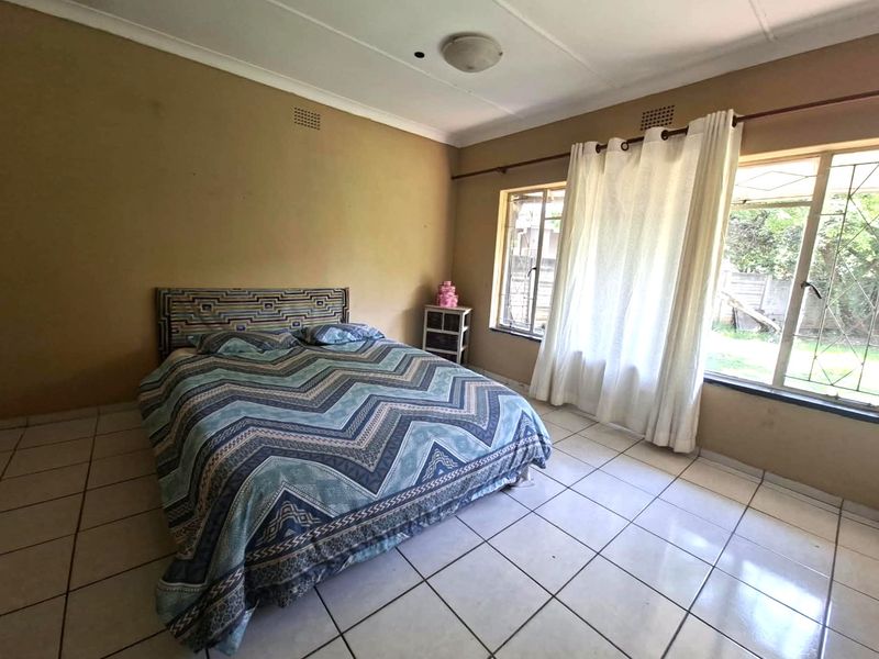A spacious bedroom featuring tiled flooring, coved ceilings, and large windows with security bars, offering a functional layout ready for cosmetic updates.