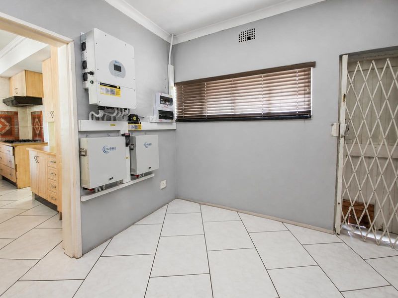 A utility space featuring a wall-mounted solar inverter and battery storage system, tiled flooring, and a security gate.