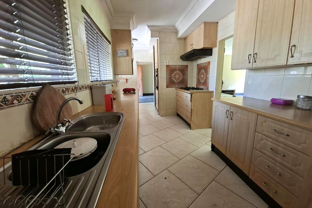 A functional kitchen featuring laminate countertops, built-in cabinetry, a gas hob with extractor fan, and tiled flooring with a classic layout.