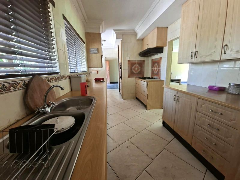 A functional kitchen featuring laminate countertops, built-in cabinetry, a gas hob with extractor fan, and tiled flooring with a classic layout.