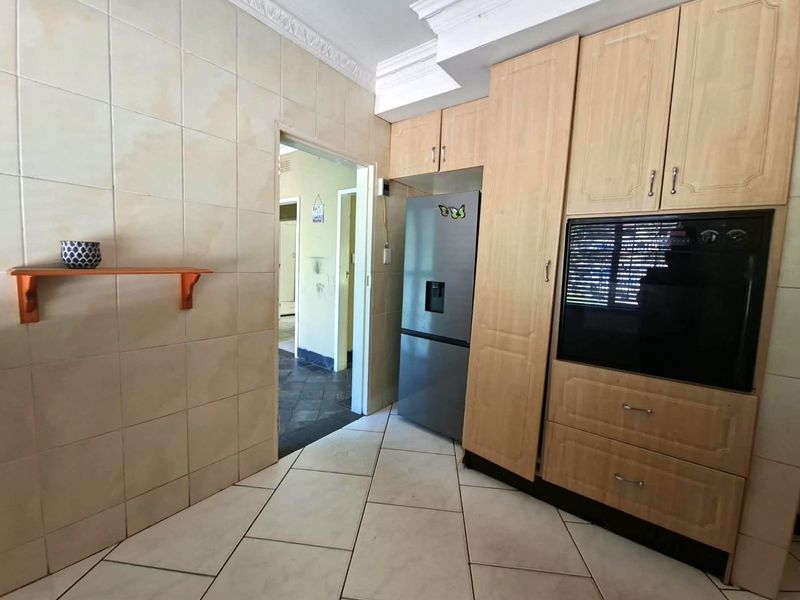 A functional kitchen featuring light wood cabinetry, built-in oven, tiled flooring, and tiled wall finishes with crown molding detail.