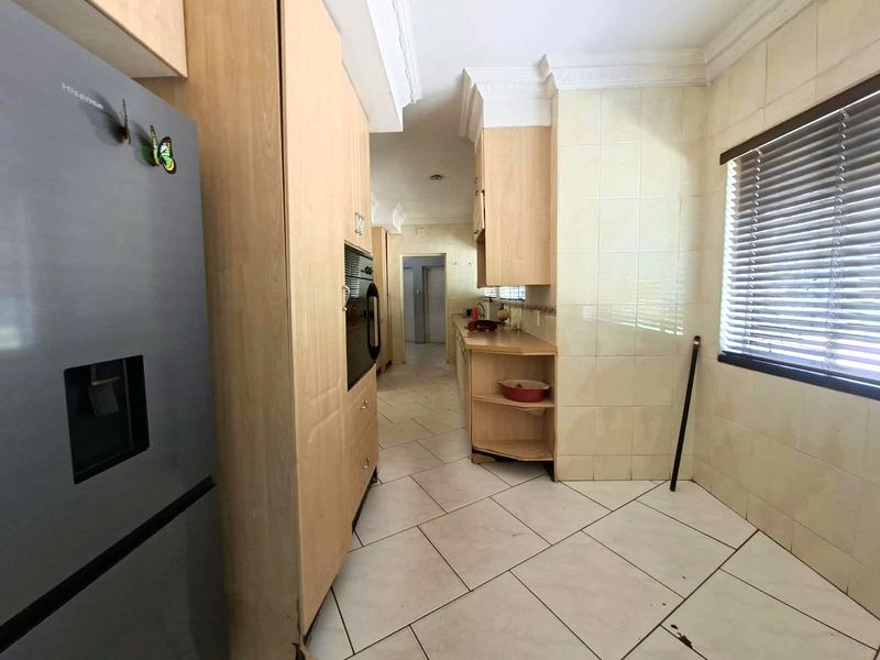 A functional kitchen featuring light wood cabinetry, tiled flooring, and a tiled splashback, offering a practical layout with built-in oven and ample storage space.