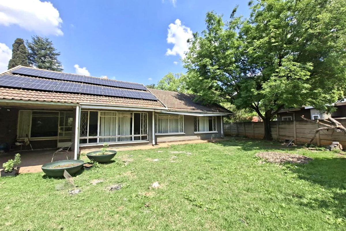Rear view of the house featuring a tiled roof with solar panels, a covered patio area, and a spacious garden with mature trees.