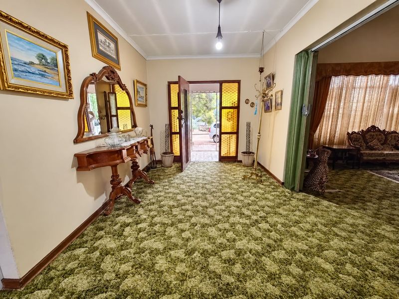 Entrance hall featuring a distinctive stained glass front door and green patterned carpeting, leading into an adjacent living area via a sliding room divider.