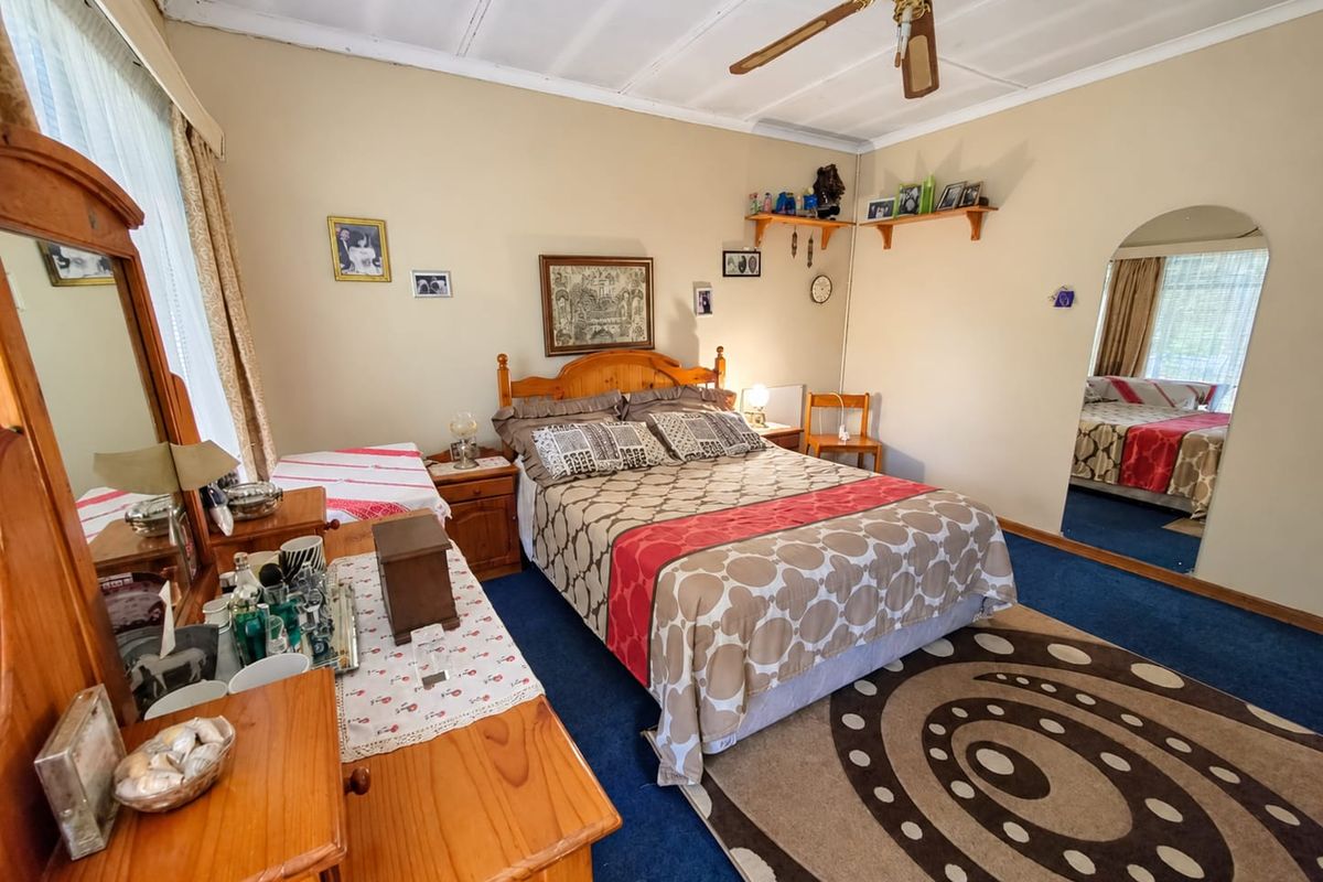 A bedroom featuring a ceiling fan, wall-mounted shelving, and a large built-in mirror, offering a functional space with potential for modernization.