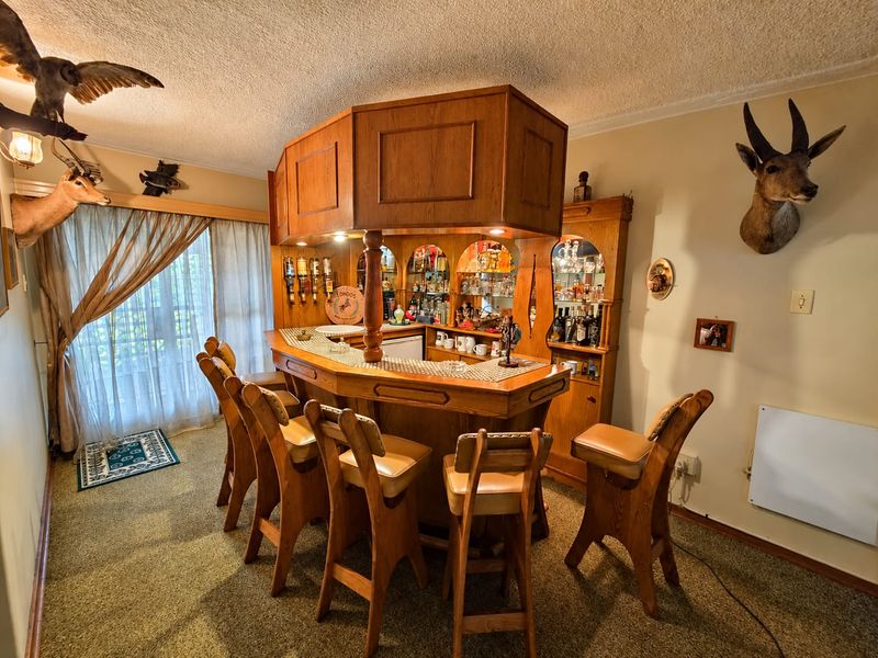A dedicated home bar area featuring a large built-in wooden bar counter with overhead canopy, integrated shelving, and direct access to a patio.