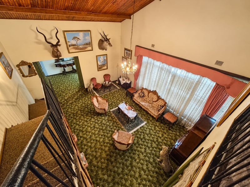 Spacious living room featuring a high vaulted timber ceiling, large windows with pelmets, and a staircase overlooking the main seating area.
