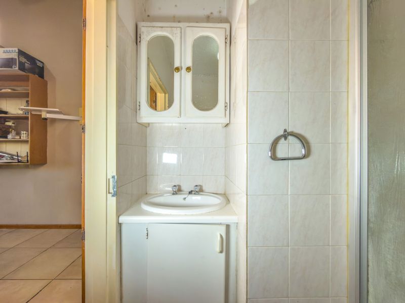 A dated bathroom featuring a vanity unit, wall-mounted medicine cabinet, and shower enclosure, requiring cosmetic updates and maintenance to address ceiling mold.