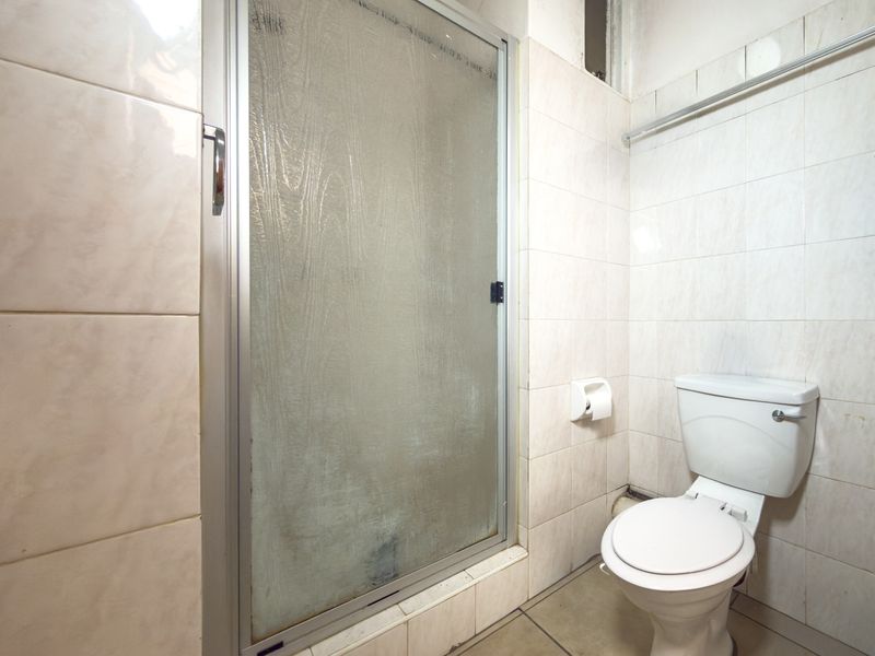 A compact bathroom featuring a shower enclosure and a standard toilet, finished with neutral ceramic wall and floor tiles.
