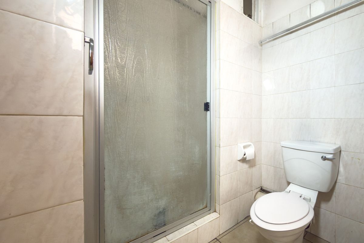 A compact bathroom featuring a shower enclosure and a standard toilet, finished with neutral ceramic wall and floor tiles.