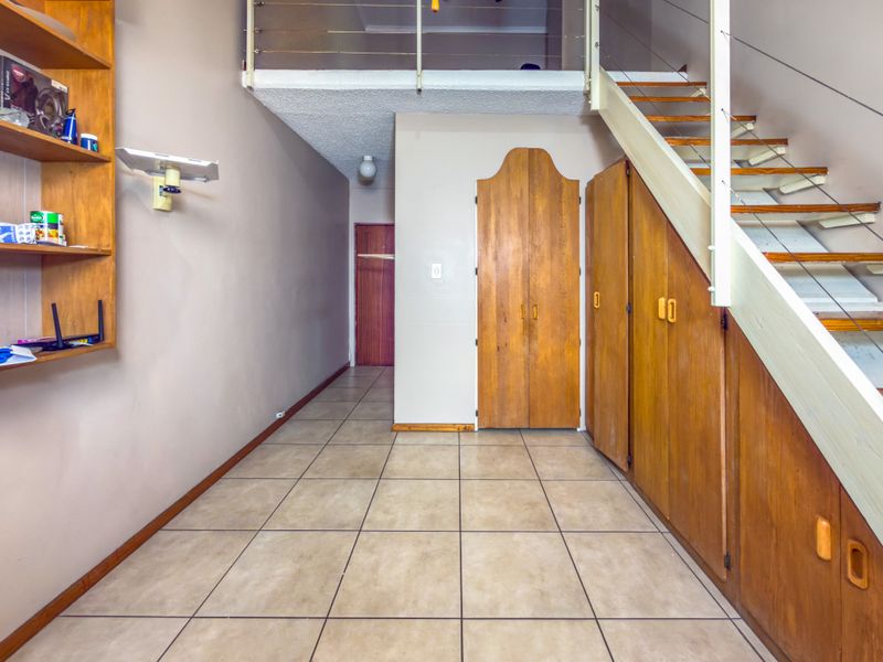An open-plan living area featuring tiled flooring, extensive built-in wooden cabinetry, and a staircase leading to a mezzanine level.