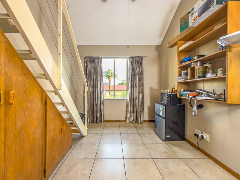 A living area featuring a staircase with integrated under-stair storage, tiled flooring, and built-in wall shelving, offering functional space with natural light.