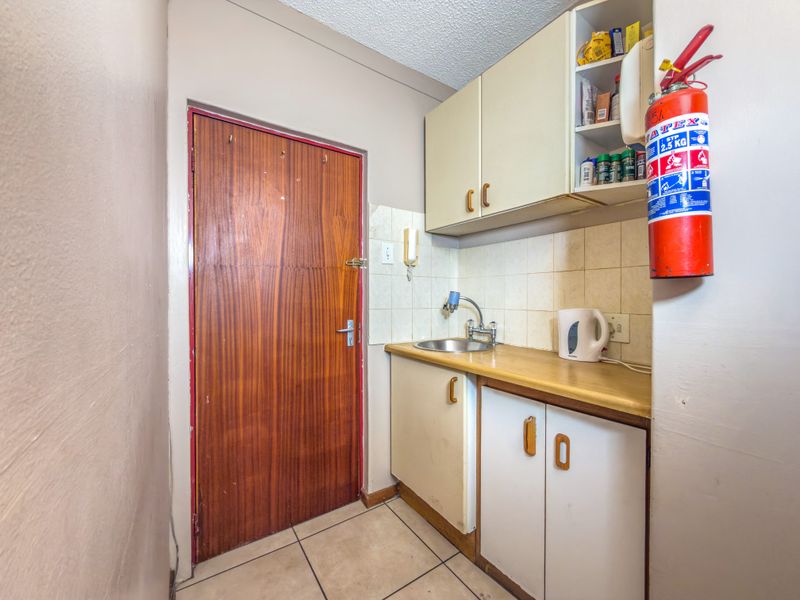 A compact scullery area featuring built-in cabinetry, a stainless steel sink, and tiled backsplash, providing functional utility space.
