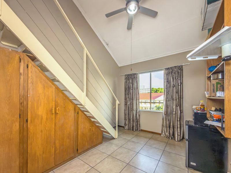Open plan living area featuring tiled flooring, a ceiling fan, and practical built-in under-stair storage cabinetry.