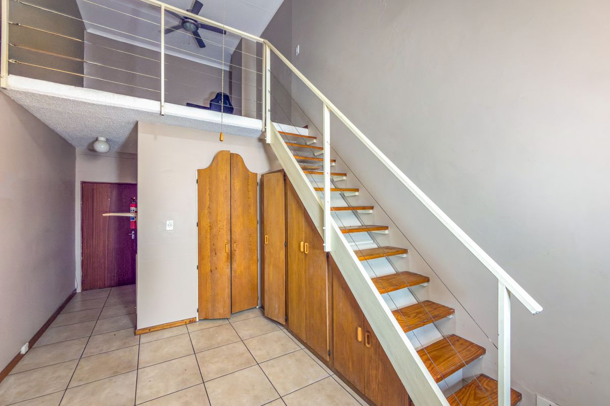 Open-plan living area featuring a mezzanine level, staircase with integrated storage cabinetry, tiled flooring, and a ceiling fan.