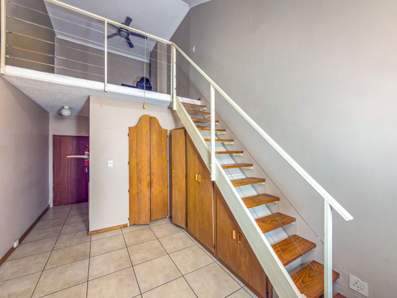 Open-plan living area featuring a mezzanine level, staircase with integrated storage cabinetry, tiled flooring, and a ceiling fan.