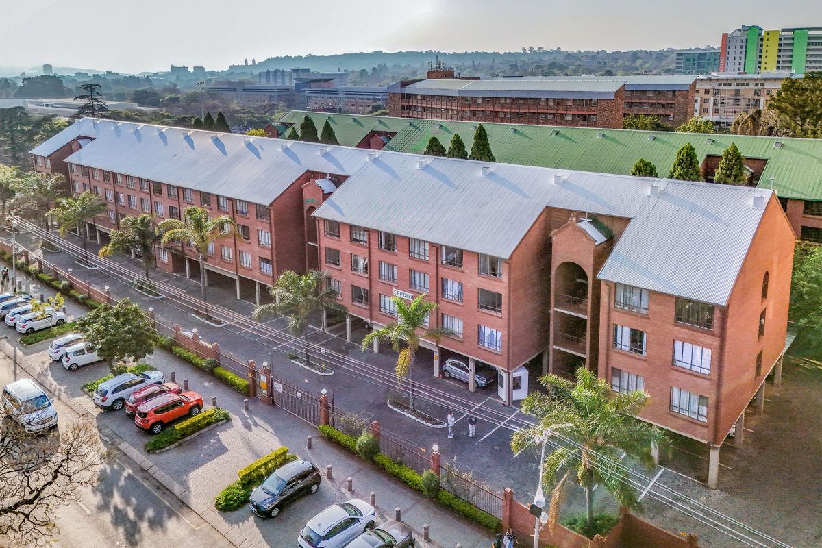 Aerial view of a multi-story brick apartment complex featuring a gated parking area, paved driveway, and established landscaping.
