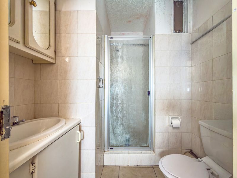 A dated bathroom featuring a shower enclosure, vanity basin, and toilet, requiring cosmetic updates and repairs to wall and ceiling finishes.