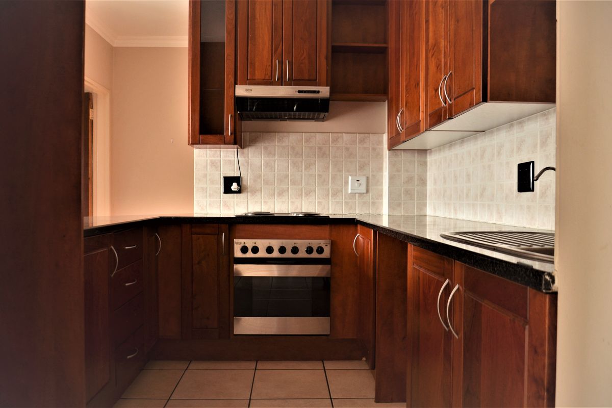 A functional kitchen featuring dark wood cabinetry, granite countertops, a built-in oven with hob, and a tiled backsplash.