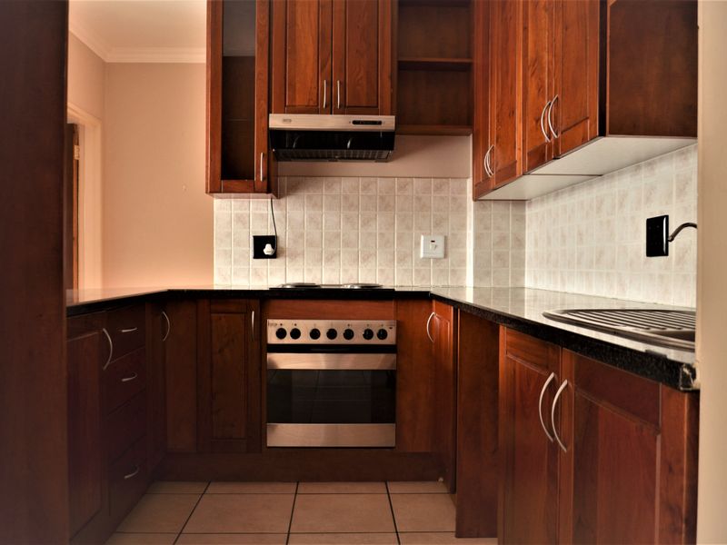 A functional kitchen featuring dark wood cabinetry, granite countertops, a built-in oven with hob, and a tiled backsplash.