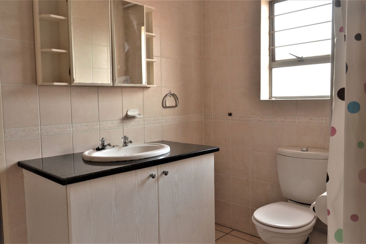 A functional bathroom featuring a vanity with granite countertop, tiled walls, and a window with security bars.