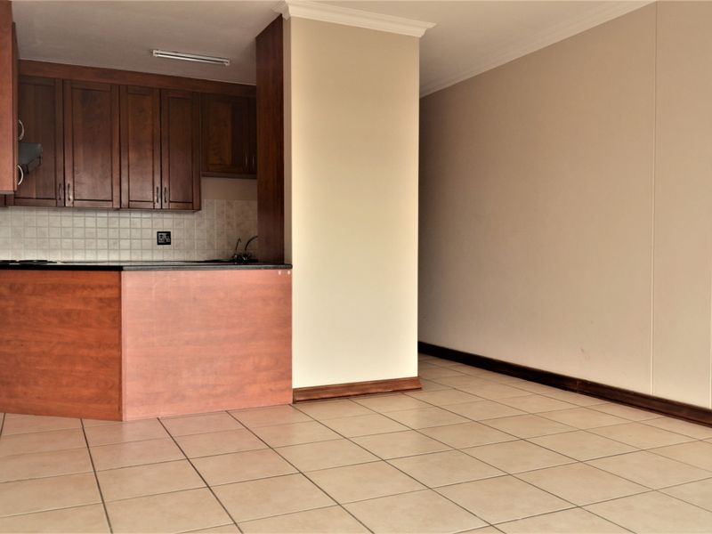 An open-plan living and kitchen area featuring tiled flooring, wooden cabinetry, and a breakfast counter, offering a blank canvas for personalization.