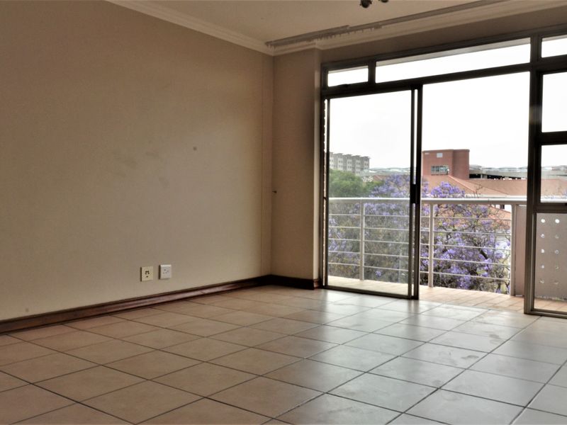 An empty living room featuring tiled flooring and a sliding glass door that opens onto a balcony with an urban view.
