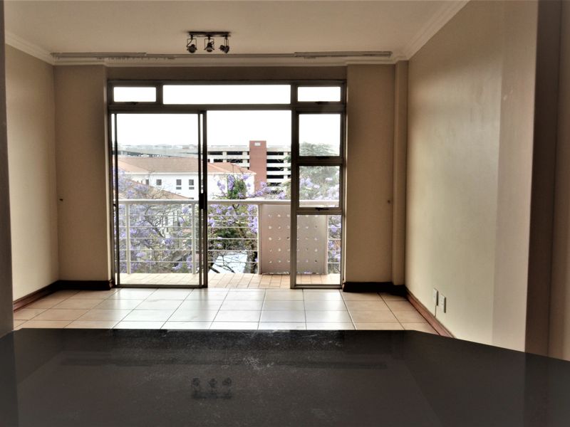 An open-plan living area featuring tiled flooring, coving, and a sliding glass door leading to a balcony with an urban view.