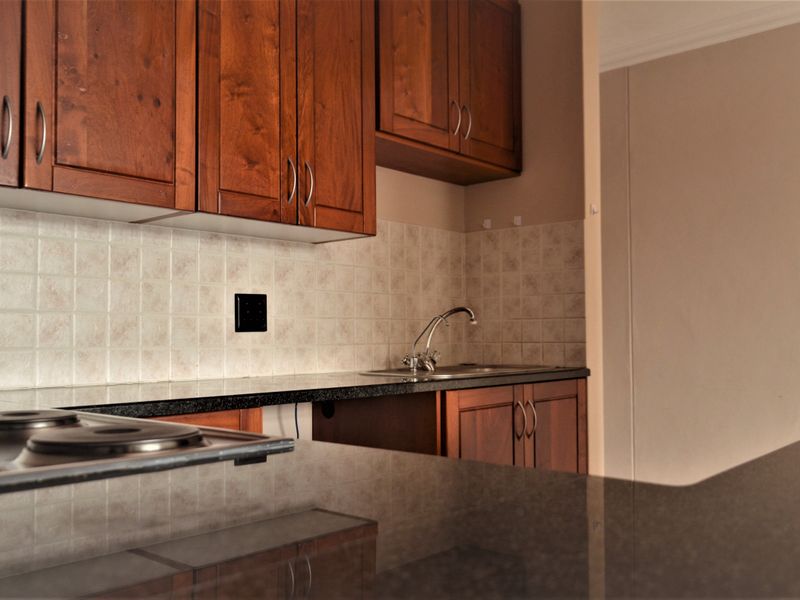 A functional kitchen featuring wooden cabinetry, granite countertops, a tiled backsplash, and a built-in electric hob.