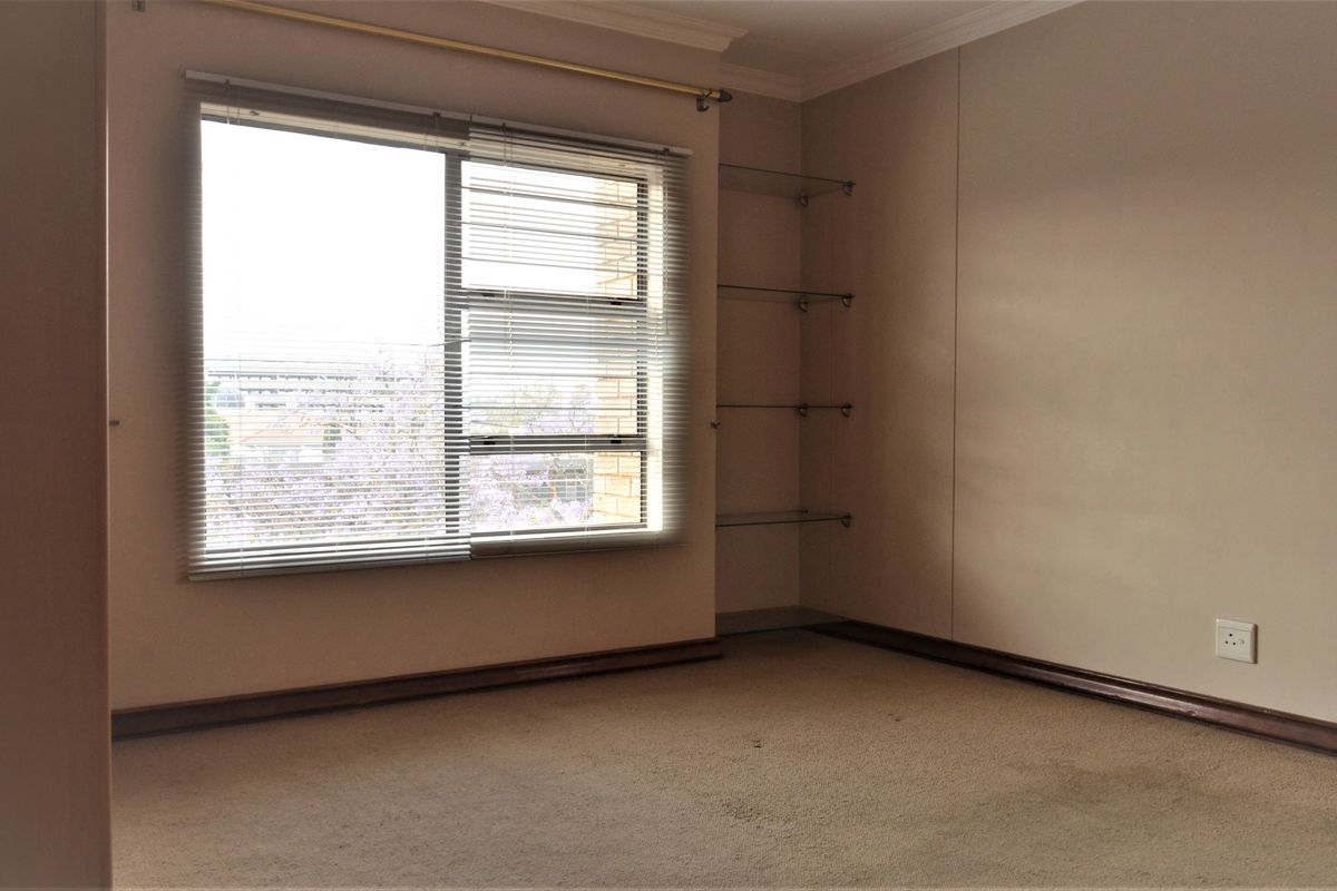 An empty bedroom featuring carpeted flooring, built-in glass shelving, and venetian blinds, offering a blank canvas for potential interior updates.