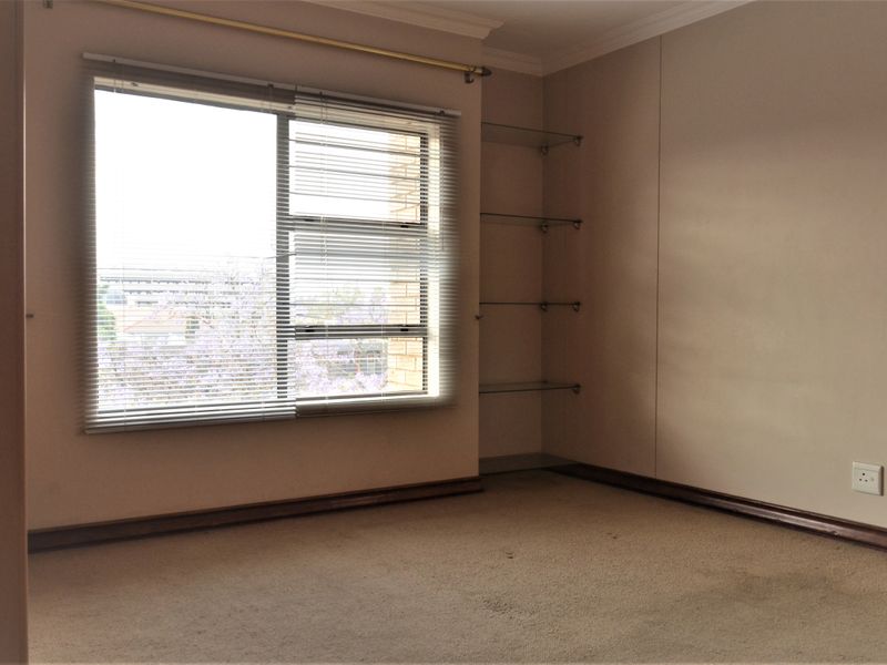 An empty bedroom featuring carpeted flooring, built-in glass shelving, and venetian blinds, offering a blank canvas for potential interior updates.