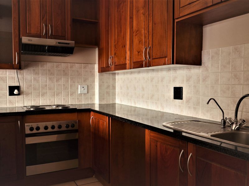 A functional kitchen featuring warm-toned wooden cabinetry, granite countertops, a built-in oven with hob, and a stainless steel sink with tiled backsplash.