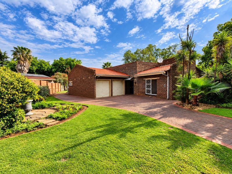 A well-maintained face brick house featuring a double garage, paved driveway, and established garden, presenting a classic and tidy street-facing facade.