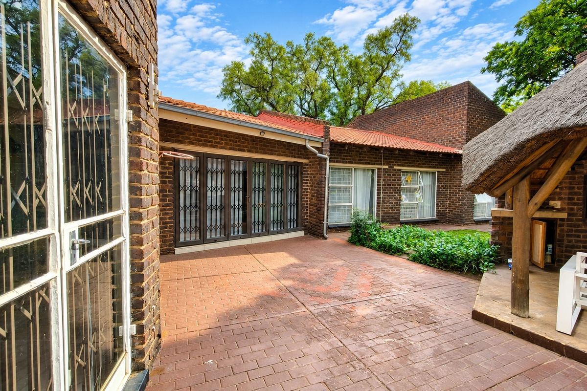 Rear exterior view featuring a paved patio area, facebrick facade, and a traditional thatch roof lapa structure.