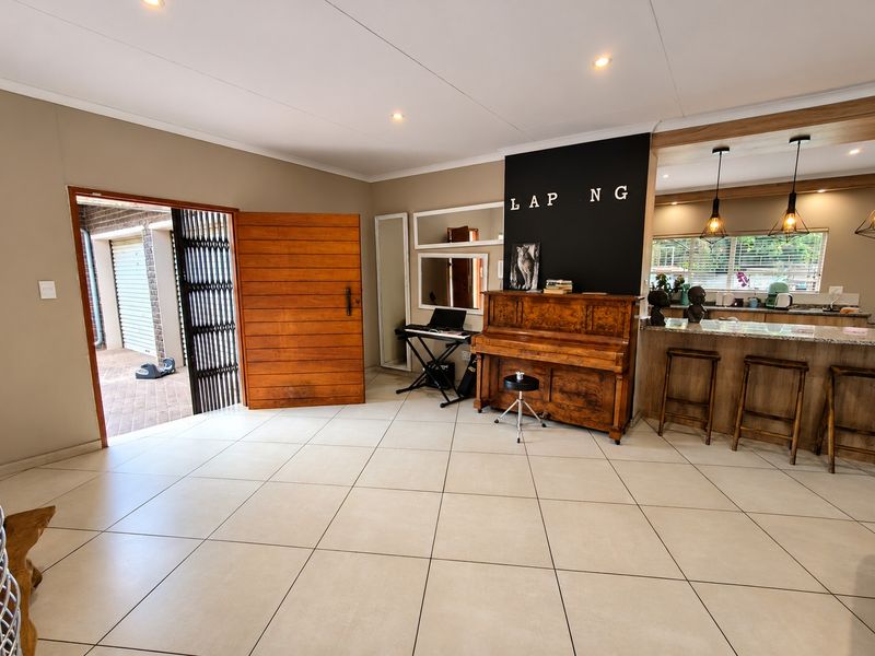 Spacious open-plan living area featuring large format floor tiles, recessed lighting, and a breakfast bar with granite countertops, seamlessly connecting to the exterior entrance.