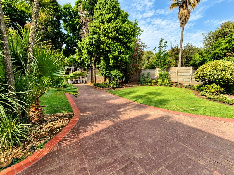 A well-maintained front entrance featuring a paved driveway, lush landscaped garden, and secure perimeter walling with a metal gate.