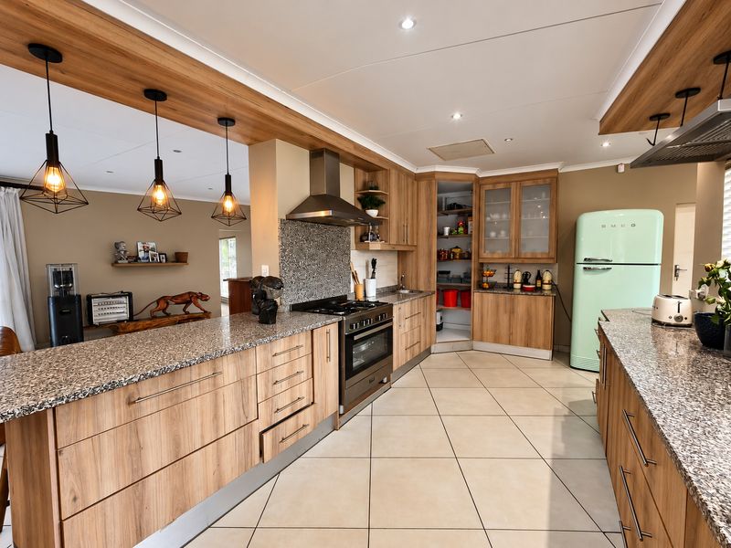 Modern kitchen featuring wood-finish cabinetry, granite countertops, a gas hob with extractor, and a convenient walk-in pantry, finished with neutral floor tiles.