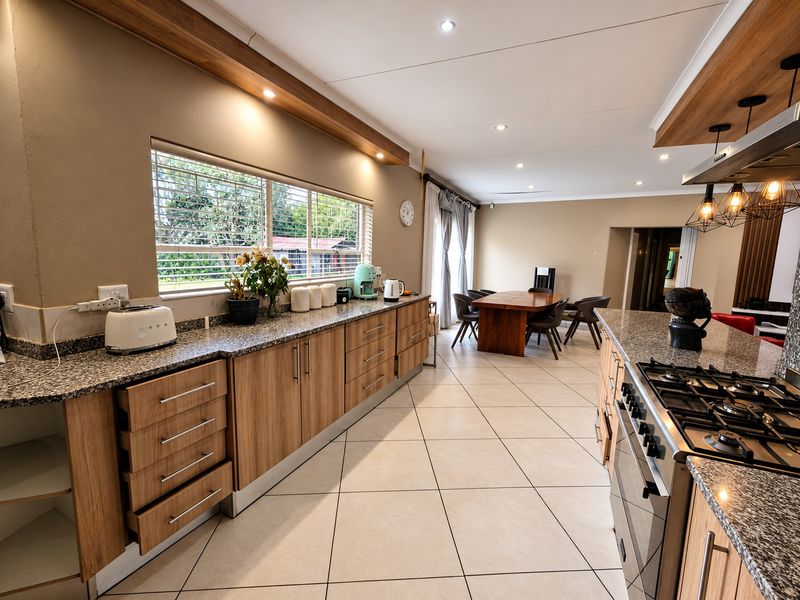 Spacious open-plan kitchen and dining area featuring modern wood-look cabinetry, granite countertops, gas hob, and tiled flooring with ample natural light.