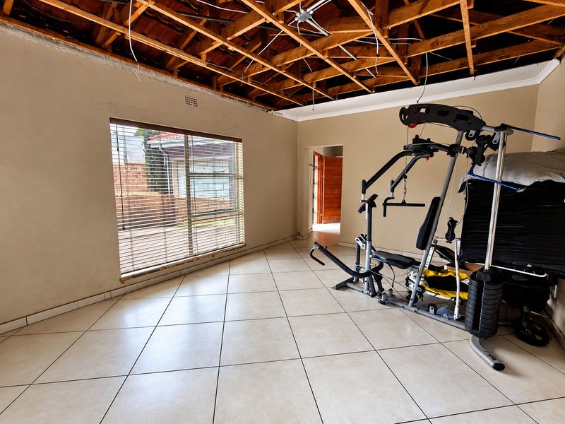 Living area featuring tiled flooring and exposed timber roof trusses, currently undergoing renovation with ceiling and electrical work required.