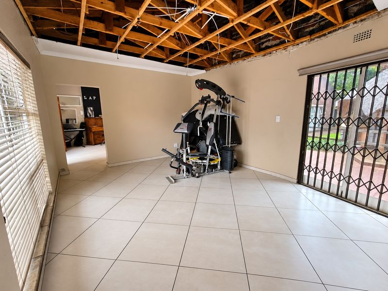 Living area featuring large floor tiles and a sliding security gate, currently undergoing ceiling repairs with exposed timber joists and wiring.