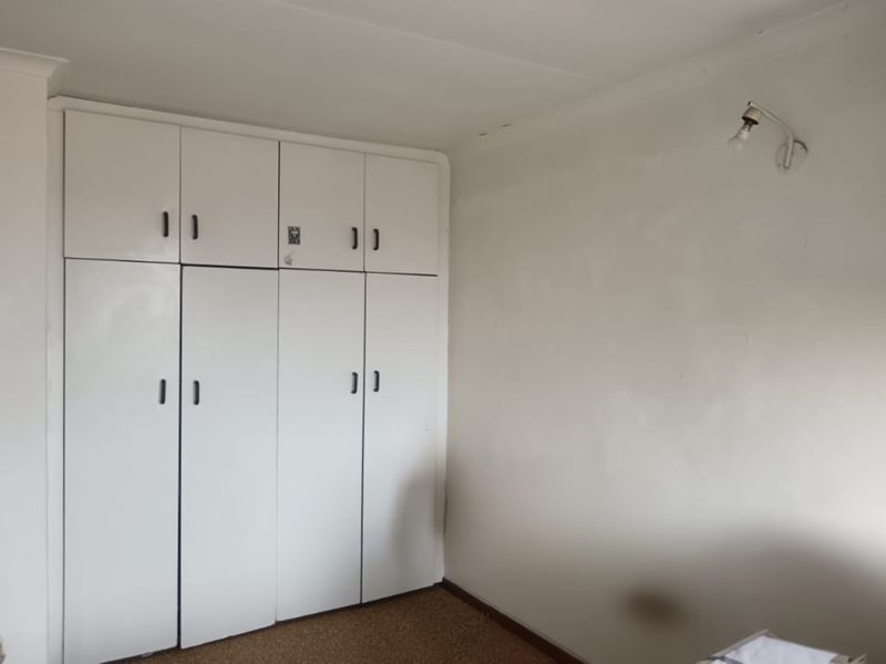 A bedroom featuring built-in cupboards, coving, and a wall-mounted light fixture, requiring cosmetic updates to the walls and flooring.