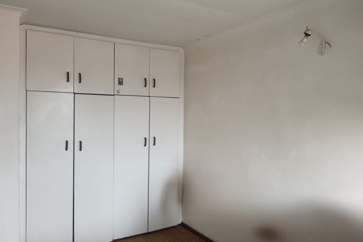 A bedroom featuring built-in cupboards, coving, and a wall-mounted light fixture, requiring cosmetic updates to the walls and flooring.