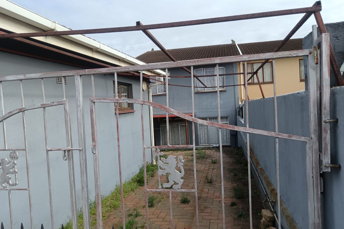 A rear courtyard area featuring paved flooring, a metal security gate, and perimeter walling, requiring maintenance and landscaping to improve the outdoor space.