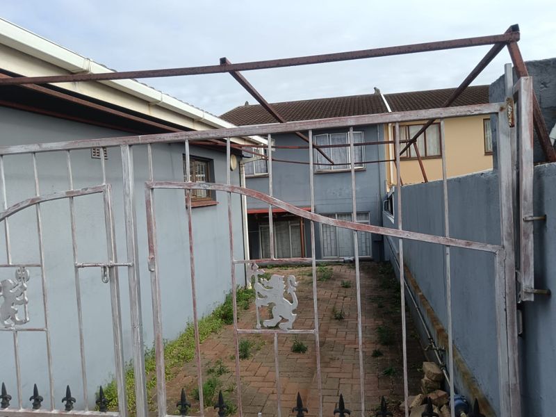 A rear courtyard area featuring paved flooring, a metal security gate, and perimeter walling, requiring maintenance and landscaping to improve the outdoor space.