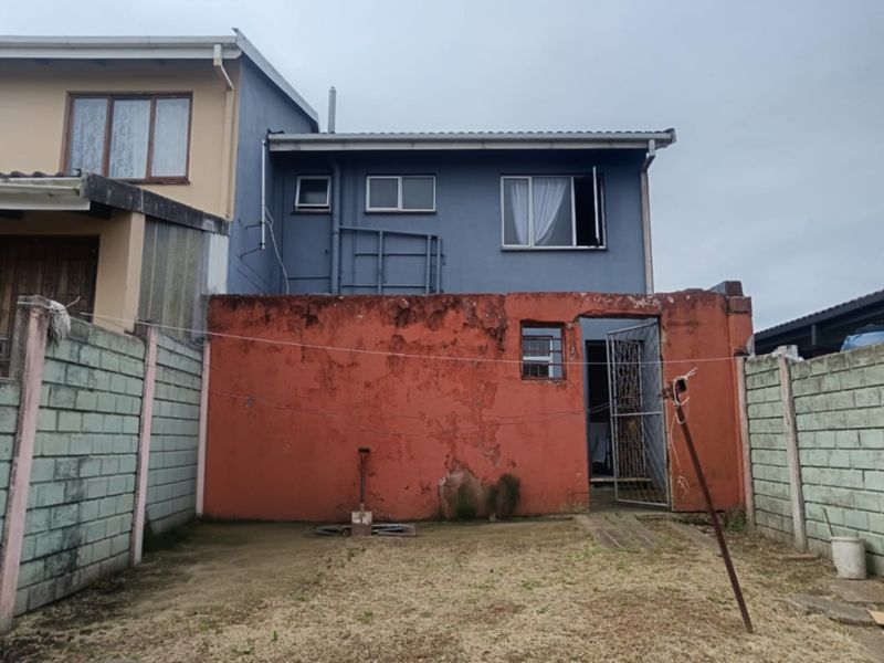 Rear view of the property featuring a small yard, concrete boundary walls, and a two-story structure with visible exterior wall weathering.