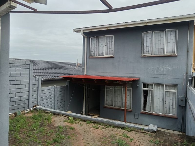 Rear view of a two-story house featuring a paved patio area, security bars on windows, and a concrete block boundary wall.